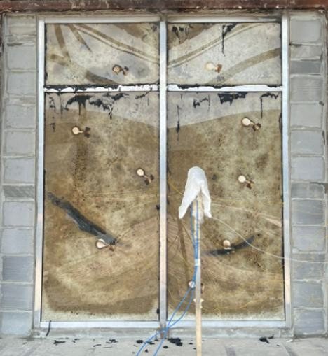 A glazed specimen in a masonry surround after a fire test, the glass darkened and discoloured across its full area, the frame still square.